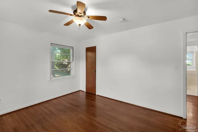 an empty room with wooden floor fan and windows