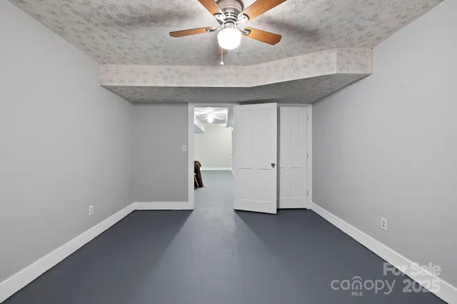 an empty room with chandelier fan and windows