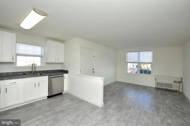 a large white kitchen with granite countertop a sink a stove a window and white cabinets
