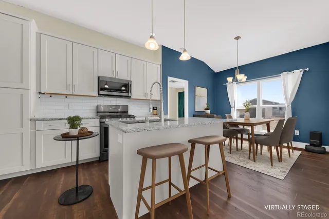 a kitchen with stainless steel appliances granite countertop a stove top oven a sink a dining table and chairs with wooden floor