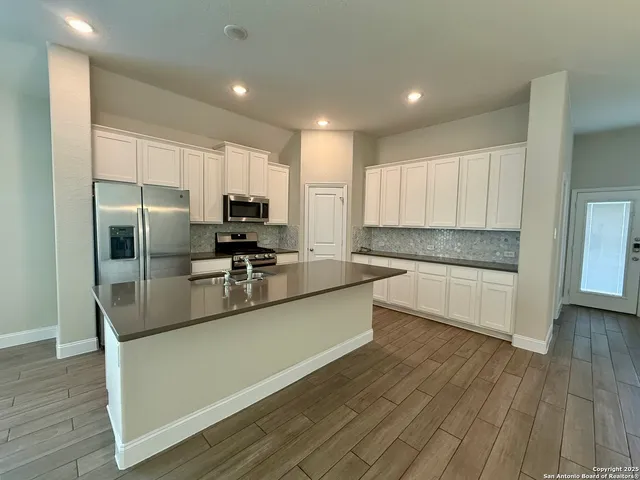 a large kitchen with stainless steel appliances granite countertop a refrigerator a stove a sink and a microwave oven with wooden floor