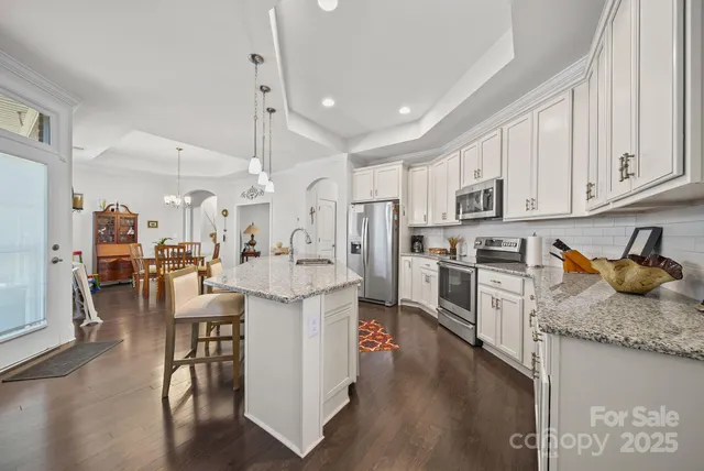 a kitchen with granite countertop lots of white cabinets a sink a stove a dining table and chairs