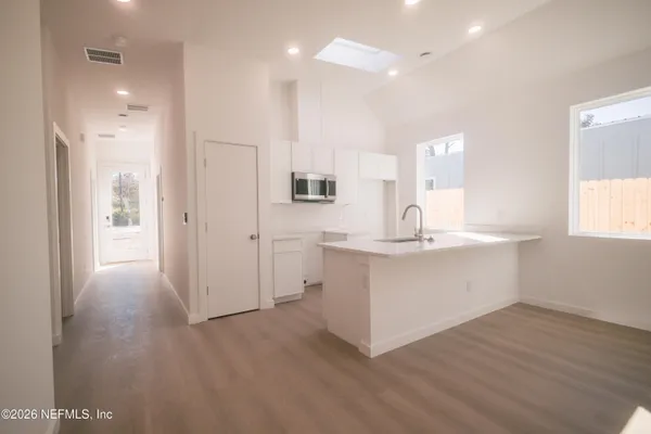 a large white kitchen with a sink a refrigerator and wooden floor