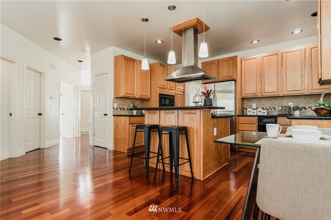 9645 South 194th Street Renton, WA 98055 - Photo 16 of 35 a kitchen with stainless steel appliances granite countertop a stove top oven a sink a dining table and chairs with wooden floor