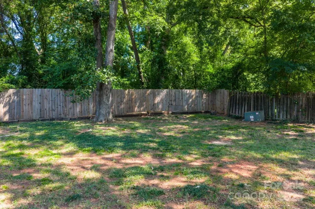 a view of a backyard with large trees and wooden fence