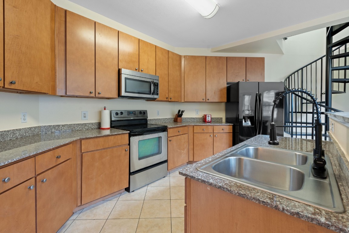 2502 Leon Street, Unit 501 Austin, TX 78705 - Photo 1 of 14 Kitchen with appliances with stainless steel finishes, light tile patterned floors, brown cabinetry, and dark countertops