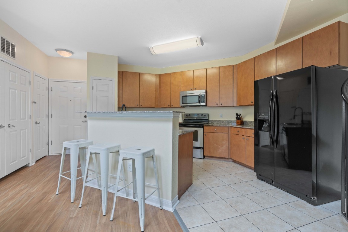 2502 Leon Street, Unit 501 Austin, TX 78705 - Photo 4 of 14 Kitchen featuring appliances with stainless steel finishes, brown cabinetry, a center island, a kitchen breakfast bar, and light wood-type flooring