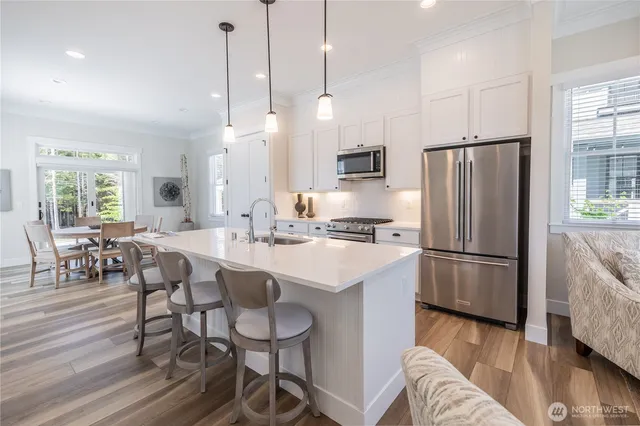 a kitchen with stainless steel appliances a refrigerator a stove a sink a dining table and chairs with wooden floor