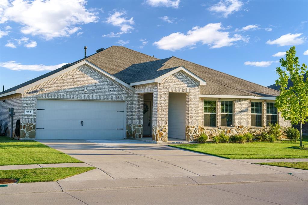 Single story home featuring an attached garage, brick siding, roof with shingles, driveway, and a front yard