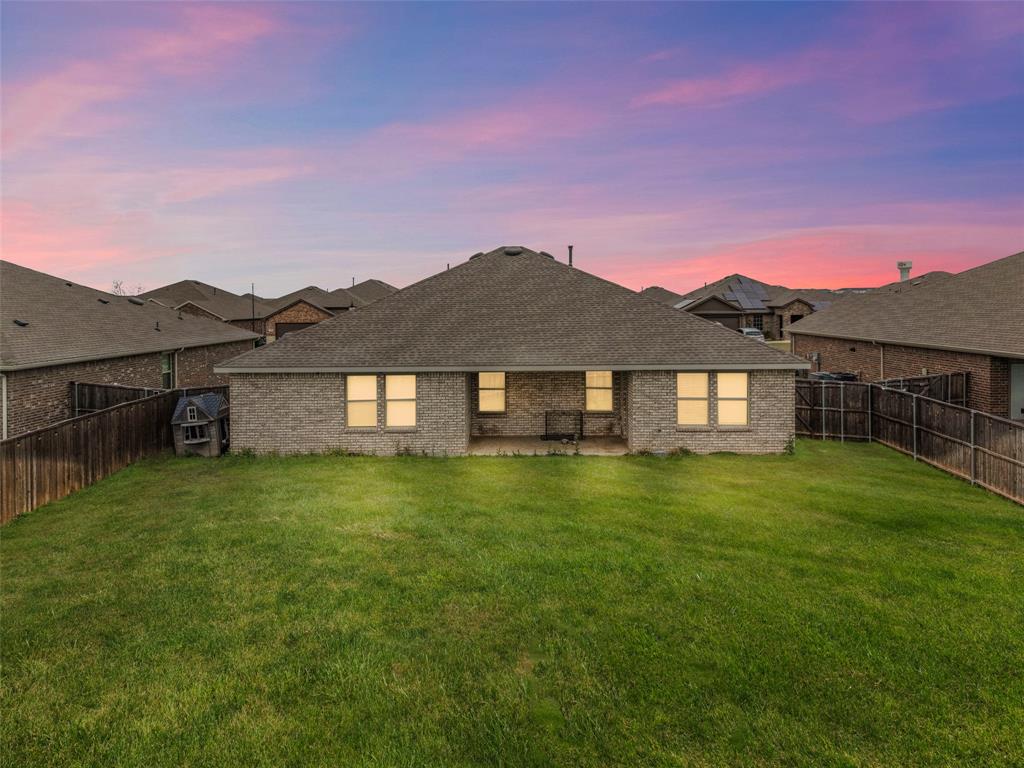 653 Bunker Hill Road Fate, TX 75189 - Photo 35 of 36 Back of house at dusk featuring a patio, a fenced backyard, brick siding, and a shingled roof
