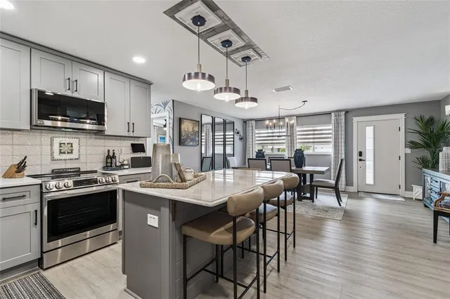 a kitchen with stainless steel appliances granite countertop a stove top oven a sink a dining table and chairs with wooden floor