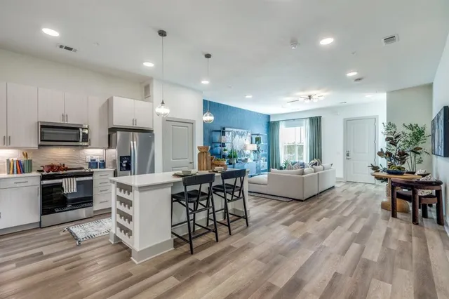 a living room with stainless steel appliances furniture wooden floor and a kitchen view
