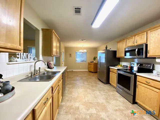 a kitchen with stainless steel appliances granite countertop a sink a stove top oven a chimney cabinets and a dining table