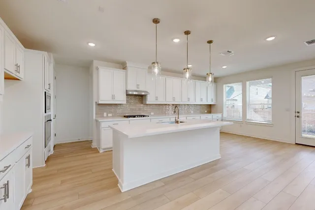 a large kitchen with stainless steel appliances a large counter top a sink a refrigerator and a window