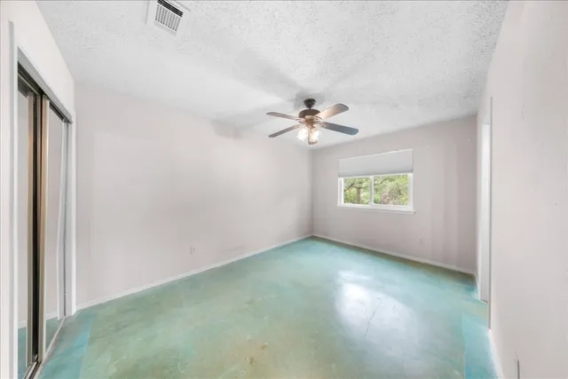 an empty room with chandelier fan and windows