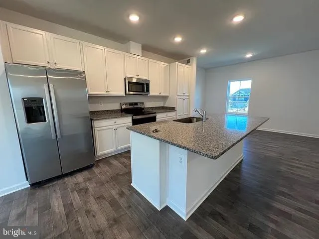 a kitchen with stainless steel appliances granite countertop a refrigerator a stove a sink a microwave a refrigerator and white cabinets