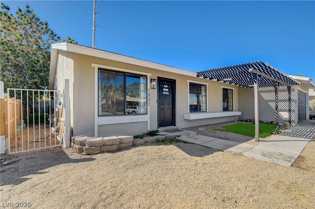 1331 Pinto Road Boulder City, NV 89005 - Photo 9 of 46 A well-maintained stucco home with a welcoming front entrance and a decorative pergola providing shade.