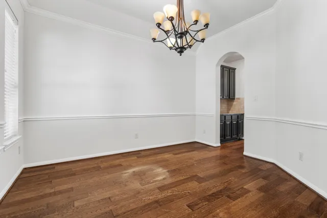 an empty room with a chandelier fan and wooden floor