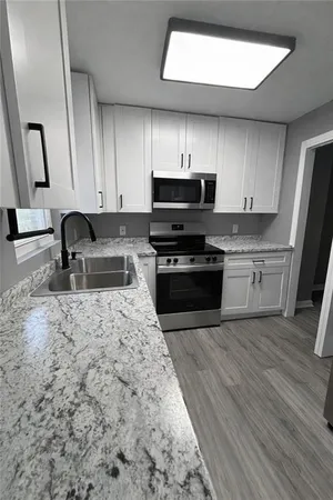 a kitchen with stainless steel appliances granite countertop a stove a sink a microwave a refrigerator a cabinets and wooden floor