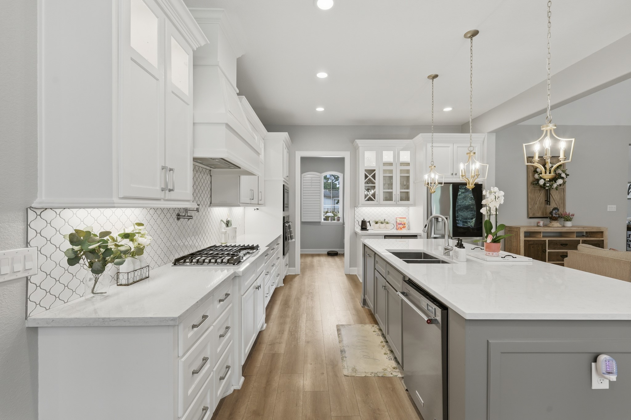 7106 Hampton Court Spring, TX 77389 - Photo 3 of 31 This kitchen features a modern design with white cabinetry, a large island with a sink, and pendant lighting. It includes a gas cooktop, stainless steel appliances, and wood flooring, creating a bright and inviting space.