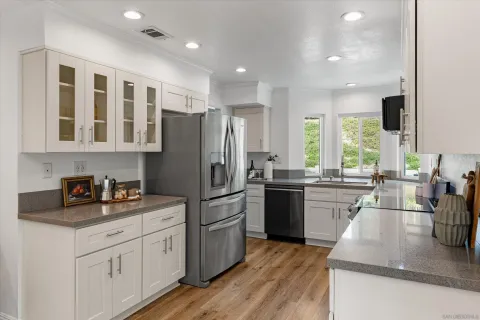 a kitchen with stainless steel appliances granite countertop a refrigerator a sink dishwasher a oven and a dining table with wooden floor