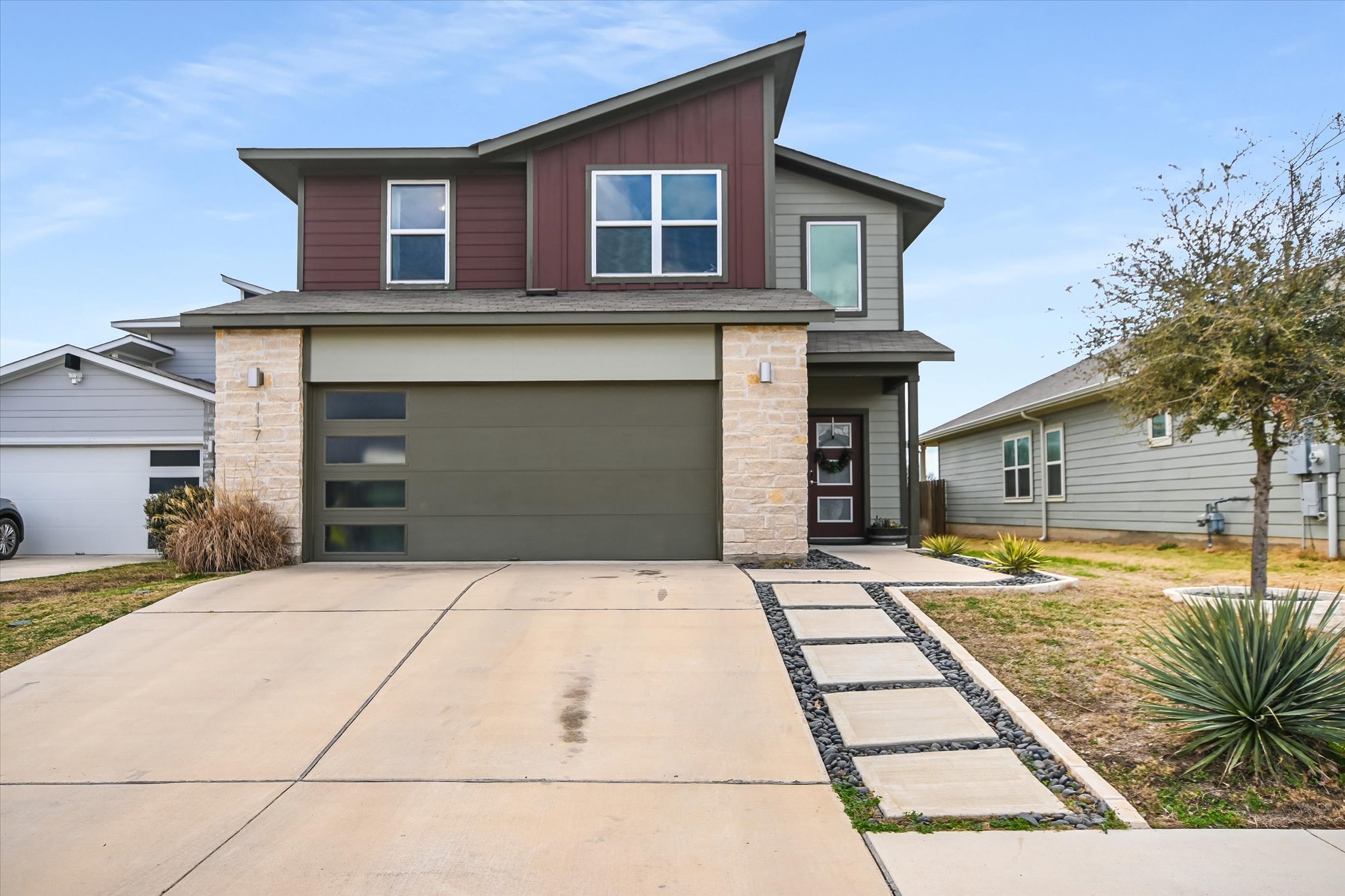 Contemporary home with stone siding, board and batten siding, driveway, and an attached garage