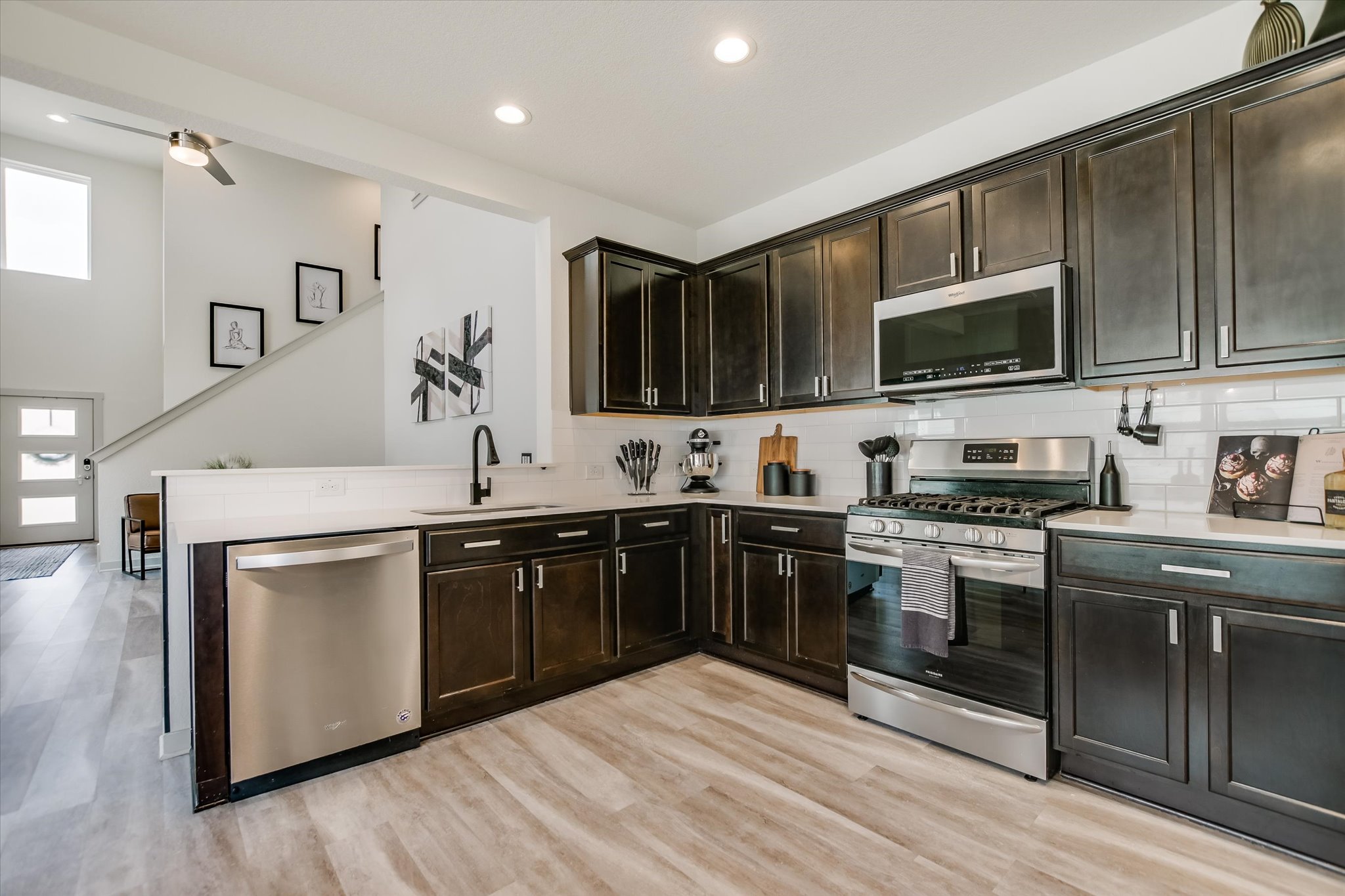 117 Deserti Road Leander, TX 78641 - Photo 9 of 21 Kitchen featuring stainless steel appliances, decorative backsplash, dark wood finish cabinetry, light wood finished floors, and recessed lighting