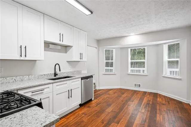 a kitchen with stainless steel appliances granite countertop a stove a sink dishwasher and white cabinets with wooden floor