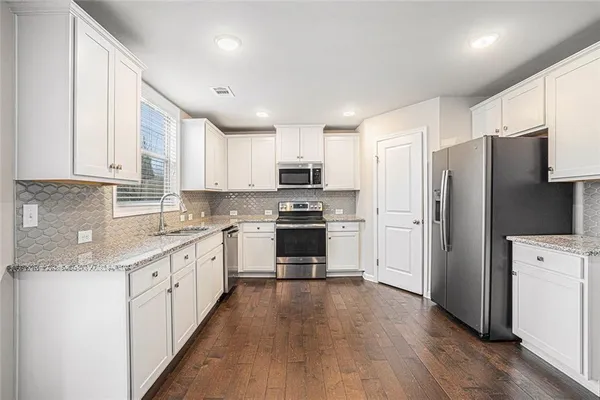 a view of an empty room with wooden floor and a kitchen