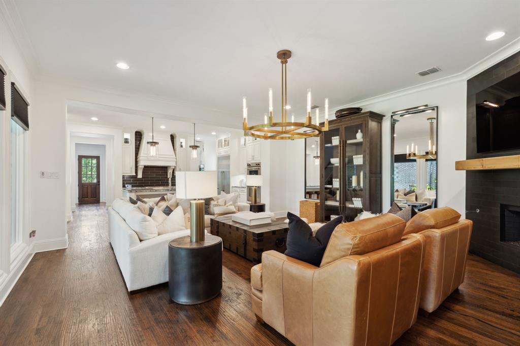 12444 Riverhill Road Frisco, TX 75033 - Photo 11 of 37 Living room with a gas fireplace, hardwood flooring, an inviting chandelier, and crown molding, lots of natural lighting with rows of windows to yard.
