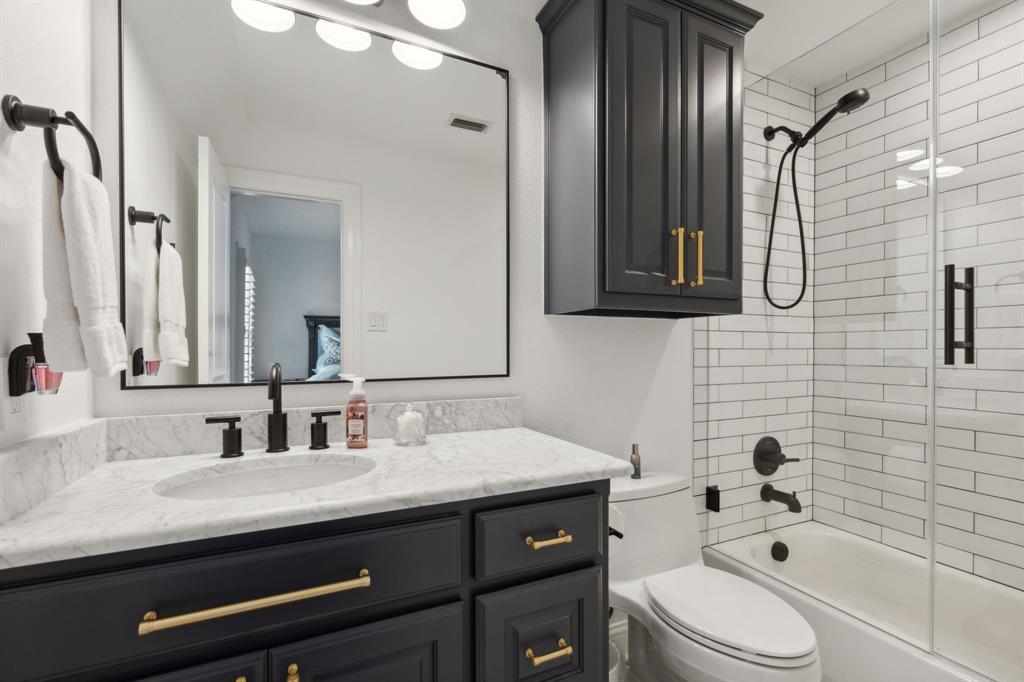 12444 Riverhill Road Frisco, TX 75033 - Photo 26 of 37 Full bathroom featuring marble vanity with extensive cabinet space, designer lighting, custom metal wrapped mirror, and tiled shower / bath with frameless glass enclosure.