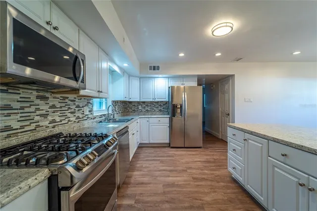 a large kitchen with kitchen island a sink dishwasher a stove and white cabinets with wooden floor