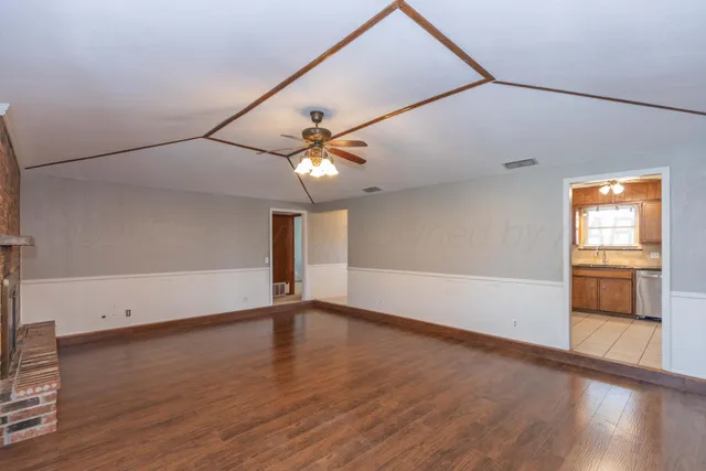 an empty room with wooden floor chandelier fan and windows