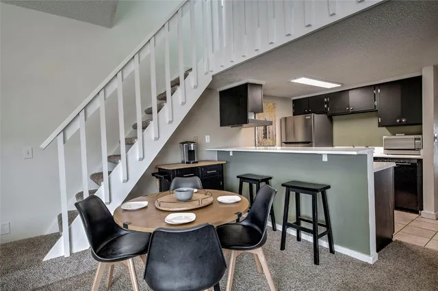 a open kitchen with stainless steel appliances kitchen island granite countertop a dining table chairs and a refrigerator