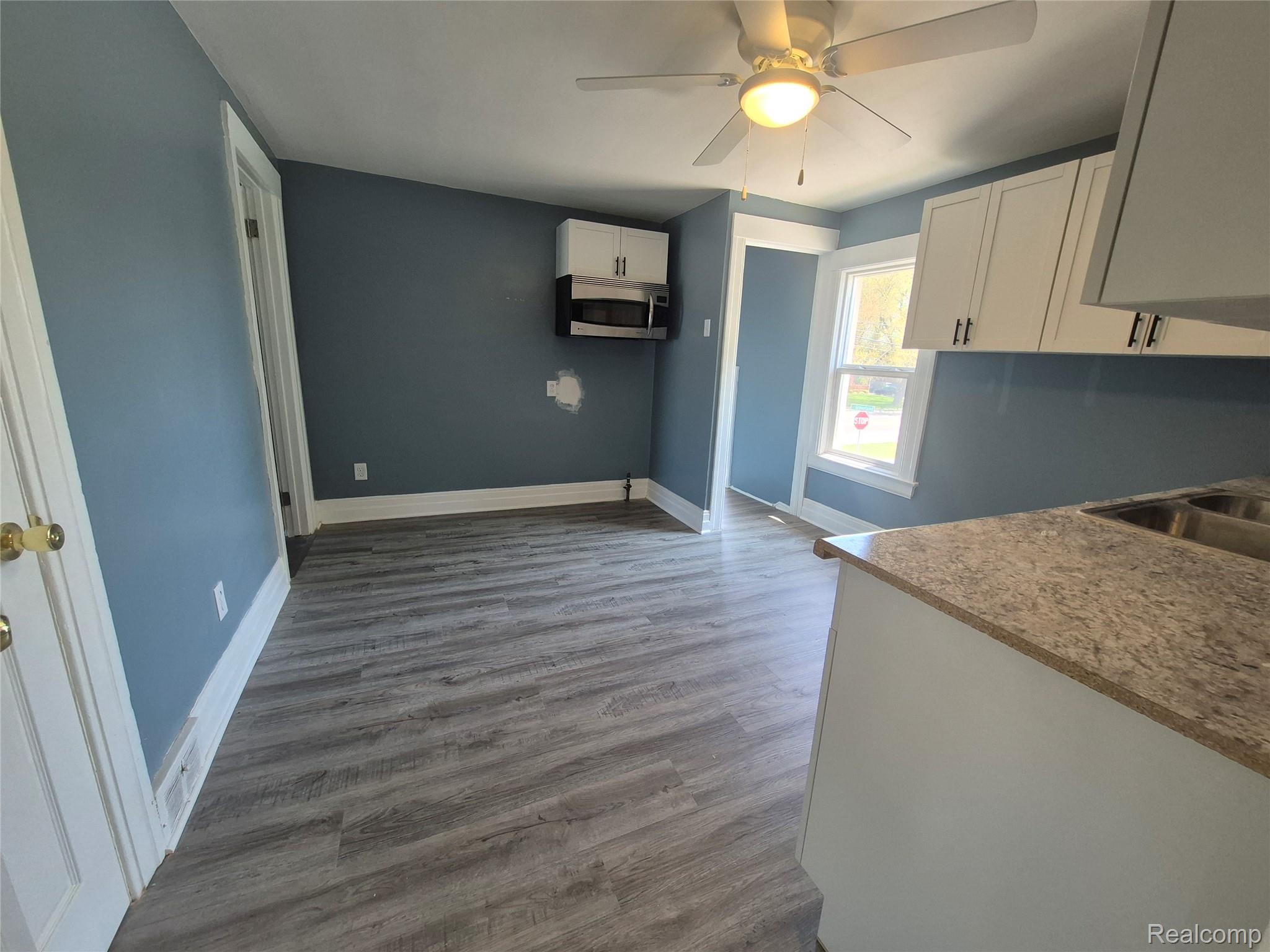 16758 Frazho Road Roseville, MI 48066 - Photo 31 of 53 Wood-finish flooring, white overhead cabinetry, ceiling fan with integrated lighting, built-in microwave, and a counter with an integrated double sink