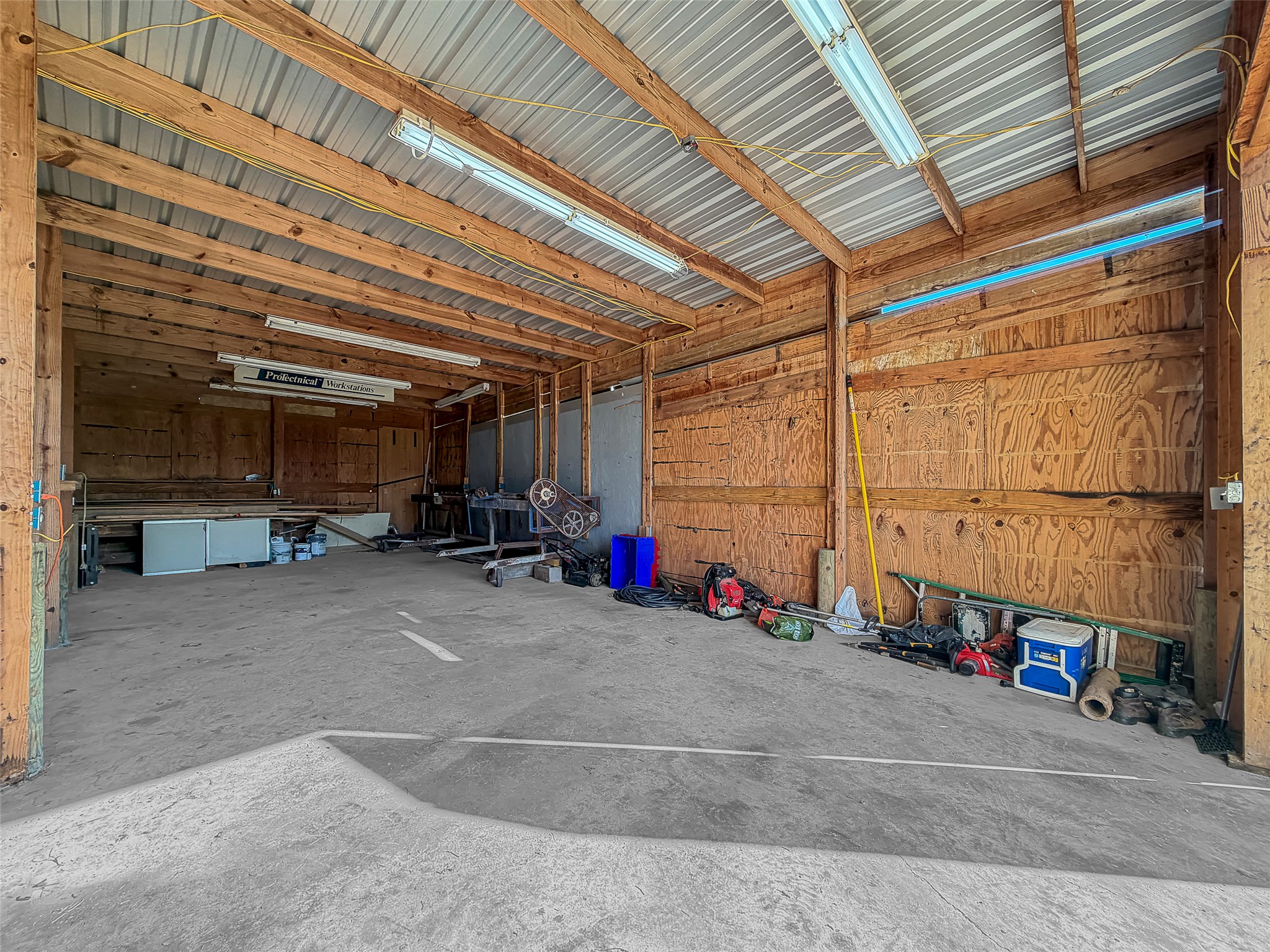925 Long Hollow Road Dale, TX 78616 - Photo 22 of 26 Spacious covered structure featuring a concrete floor, exposed wood beam construction, plywood walls, and fluorescent lighting fixtures