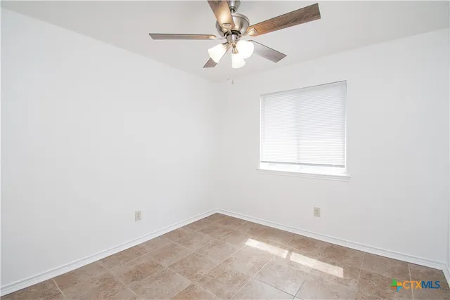 an empty room with a chandelier fan and windows