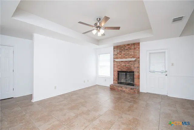a view of an empty room with chandelier fan and fire place