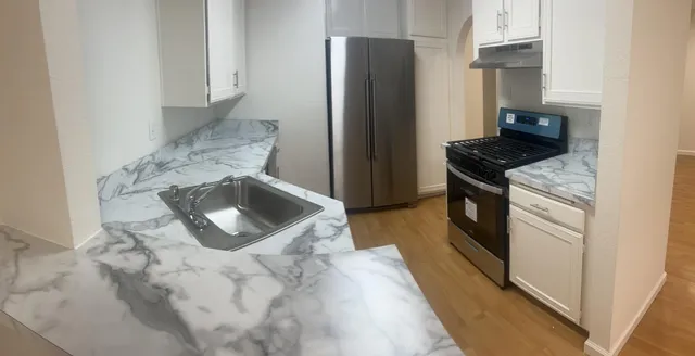 a kitchen with stainless steel appliances granite countertop a refrigerator a stove and a sink with wooden floors