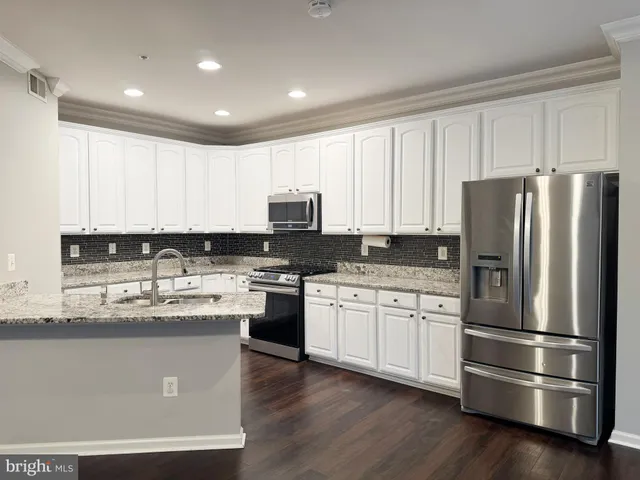 a kitchen with stainless steel appliances granite countertop a refrigerator stove a sink and white cabinets