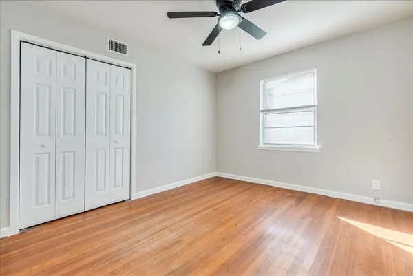 an empty room with wooden floor fan and windows