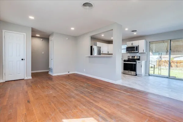 an empty room with wooden floor and stainless steel appliances