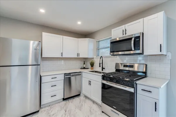 a kitchen with stainless steel appliances white cabinets and a stove a refrigerator a sink