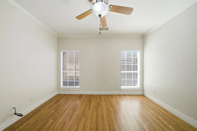 an empty room with wooden floor chandelier fan and windows