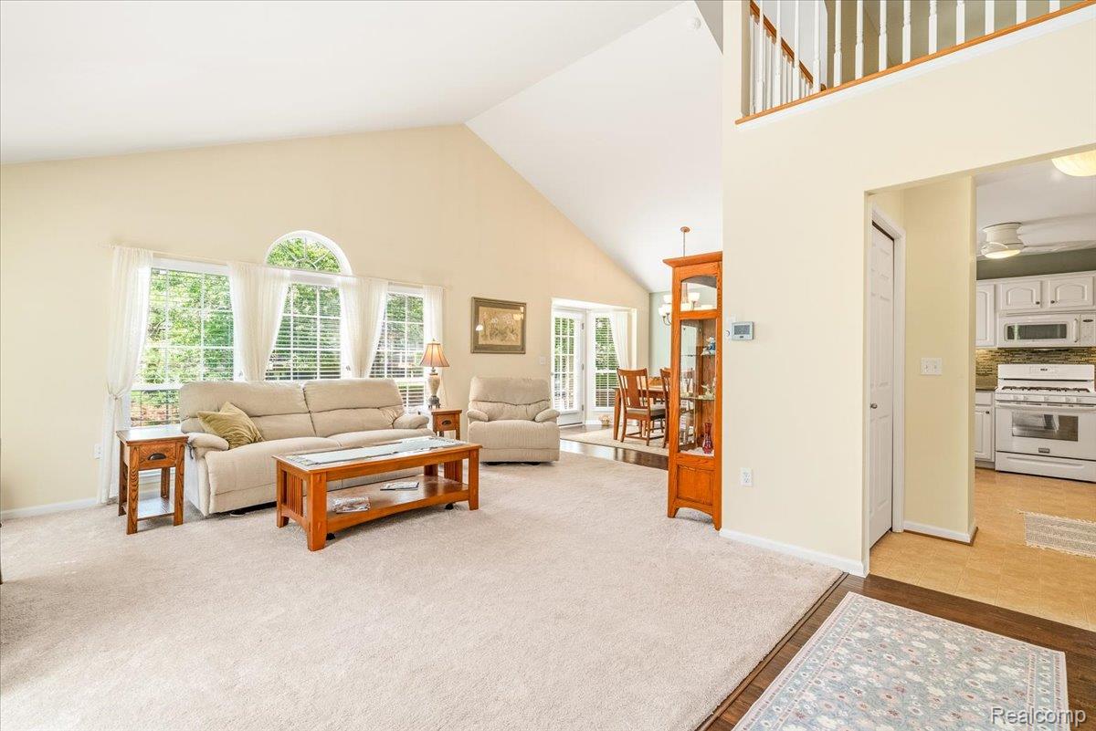 49105 Hawksburry Road Canton, MI 48188 - Photo 3 of 51 Vaulted ceiling living area featuring a trio of large windows with an arched transom, a carpeted floor, and a second-story interior balcony with white balusters