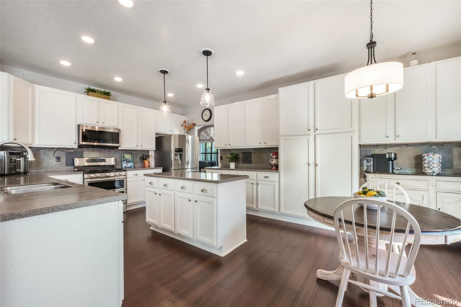 4457 Centerville Drive Colorado Springs, CO 80922 - Photo 15 of 50 a kitchen with stainless steel appliances kitchen island granite countertop a stove a sink a refrigerator a microwave oven with white cabinets and wooden floor