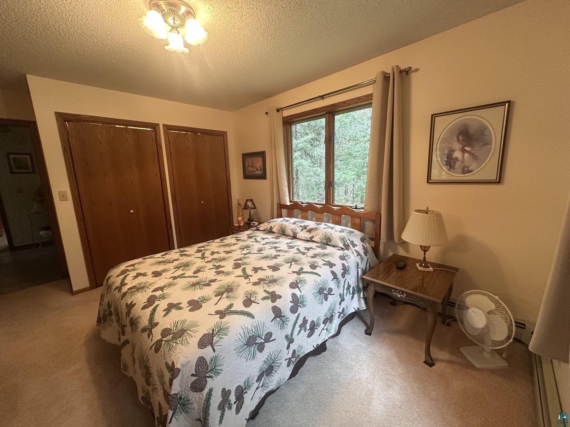 81 Hautaluoma Road Esko, MN 55733 - Photo 14 of 43 Carpeted room featuring a double window with a wooded backdrop, two wood-finish bi-fold closet doors, and a ceiling-mounted light fixture