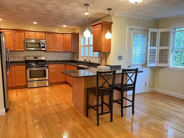 a kitchen with stainless steel appliances kitchen island granite countertop a stove a sink a dining table and chairs with wooden floor