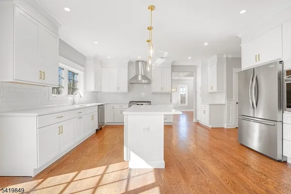 a kitchen with stainless steel appliances granite countertop a refrigerator a sink dishwasher a stove and white cabinets with wooden floor