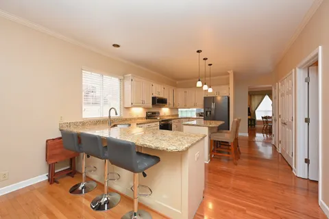 a kitchen with stainless steel appliances granite countertop a stove a sink a center island a refrigerator wooden floor and a view of living room